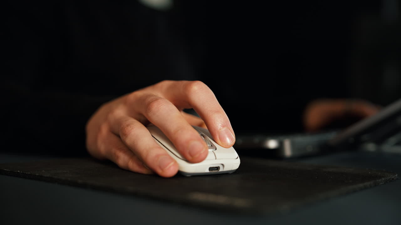 Close-up of a person using a computer mouse beside a laptop at home. Perfect for themes of remote work, office lifestyle, freelance jobs, technology, and digital communication