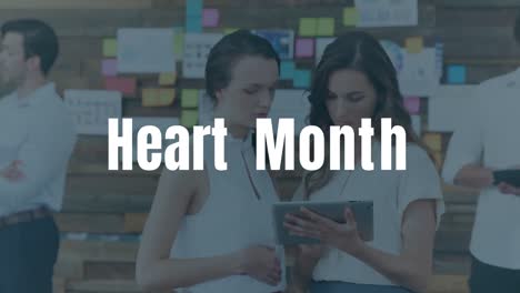 Herzmonat-Textbanner-über-Zwei-Kaukasischen-Kolleginnen,-Die-Im-Büro-Ein-Digitales-Tablet-Nutzen