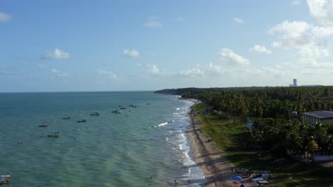 Dolly-In-Einer-Drohnenaufnahme-Der-Wunderschönen-Tropischen-Küste-Von-Penha-In-Der-Nähe-Der-Hauptstadt-Joao-Pessoa-In-Paraiba,-Brasilien,-Mit-Wellen,-Die-In-Den-Sand-Krachen,-Und-Kleinen-Angedockten-Fischerbooten