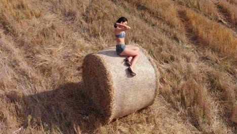 orbital shot of pretty young woman playing with her hair while sitting in bale of hay