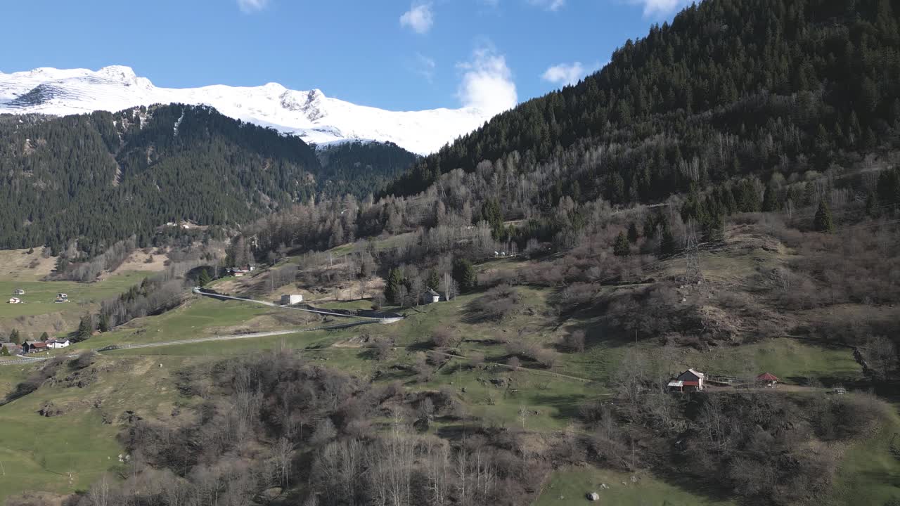 снимок с дрона, склоны швейцарских альп, деревня в зеленых холмах под заснеженными вершинами