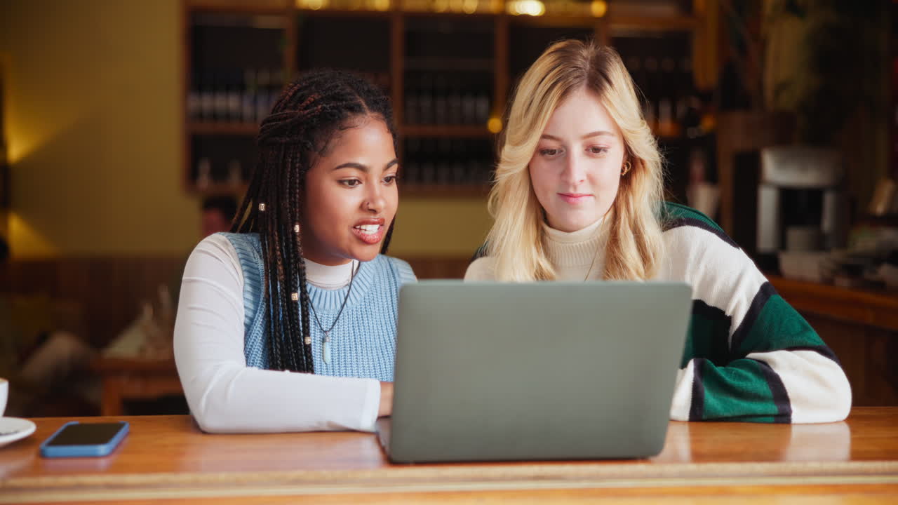 Two friends working on a laptop in a cafe