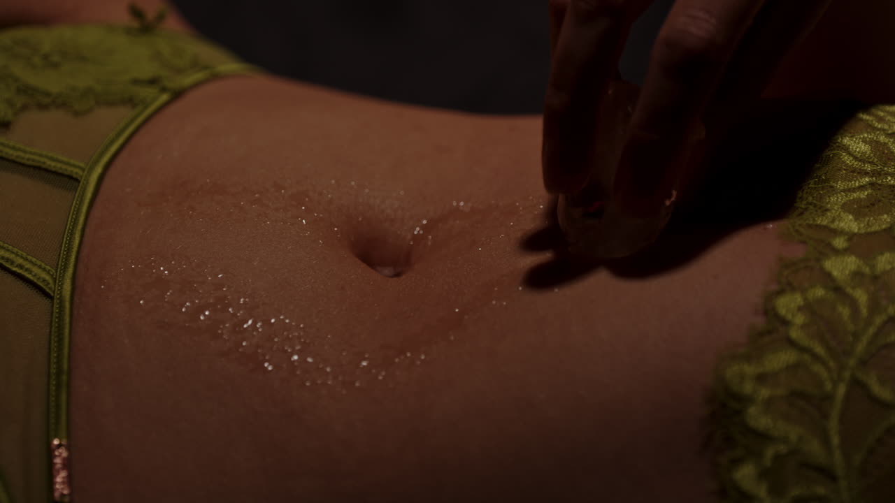 Cinematic close up of a cold ice cube being rubbed on the bare belly of a beautiful woman in a black room