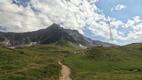 Vistas-A-Los-Postes-De-Energía-En-Un-Valle-Verde-De-Gran-Altitud-Frente-A-Las-Montañas-De-Los-Alpes-En-Suiza