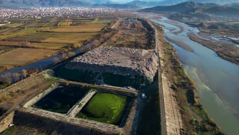 Landfill-with-huge-waste-mountain-near-the-river-and-agricultural-land-with-Elbasan-cityscape-background-in-Albania