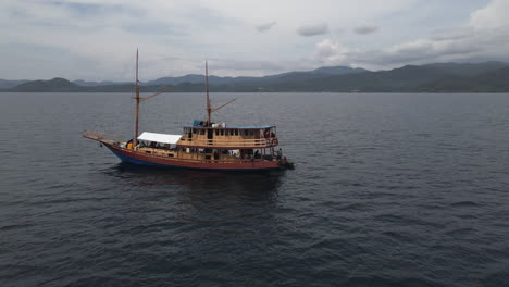 Drone-Orbiting-At-Wooden-Boat-Carrying-Tourists-Sailing-At-Calm-Ocean-In-Bali,-Indonesia