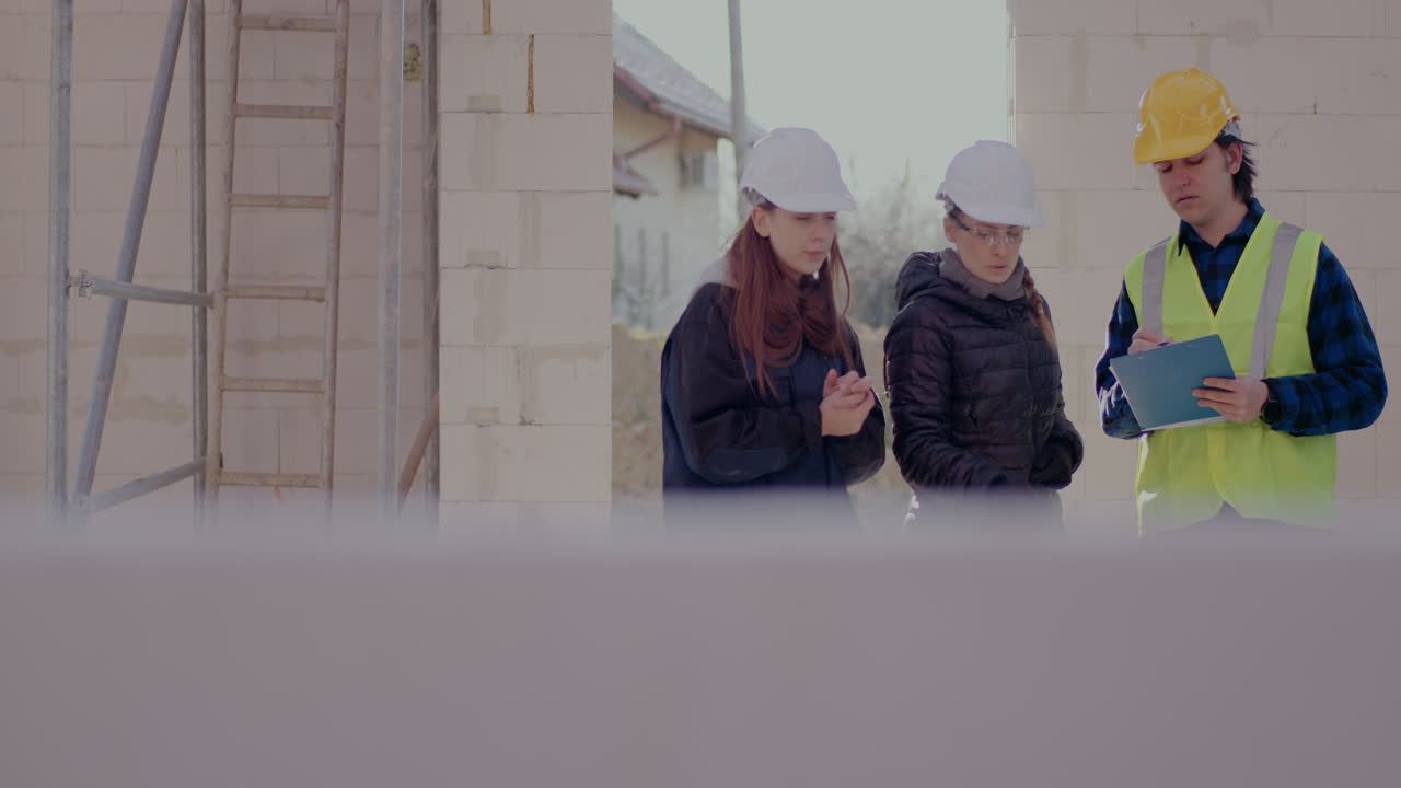Lockdown shot of confident young female engineer discussing over clipboard with supervisor and worker standing together at construction site