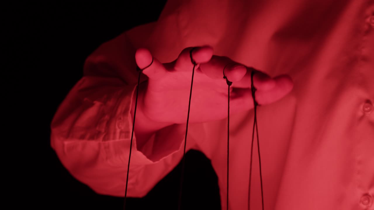 Human Hand Manipulating Puppet Strings Under Dramatic Red Light