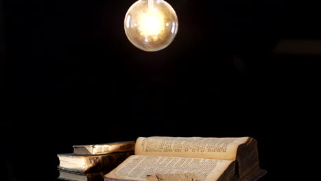 antique books on table desk in dark room illuminated by light bulb,sliding dolly shot