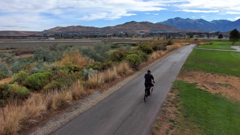 mature man going for a ride on a bicycle on a paved path through a city park - aerial tracking view