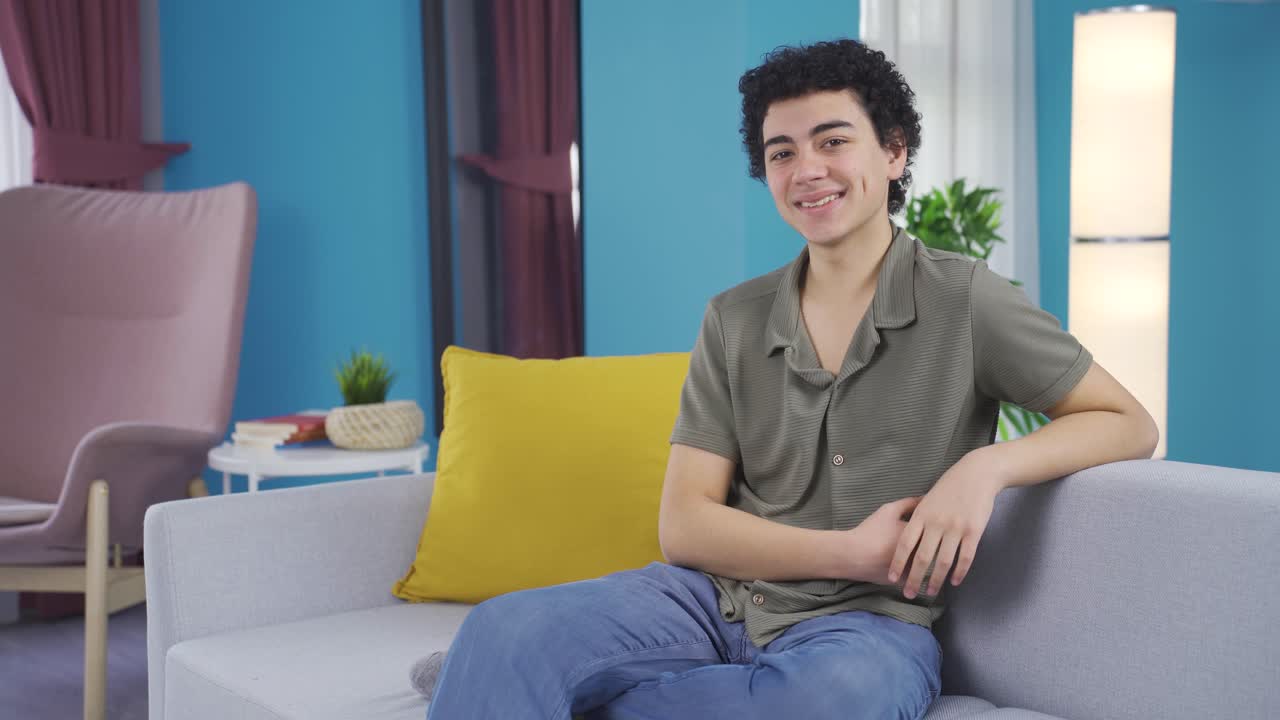 젊은 소년은 카메라와 기계에 미소를 지으며 긍정적인 몸짓을 합니다.