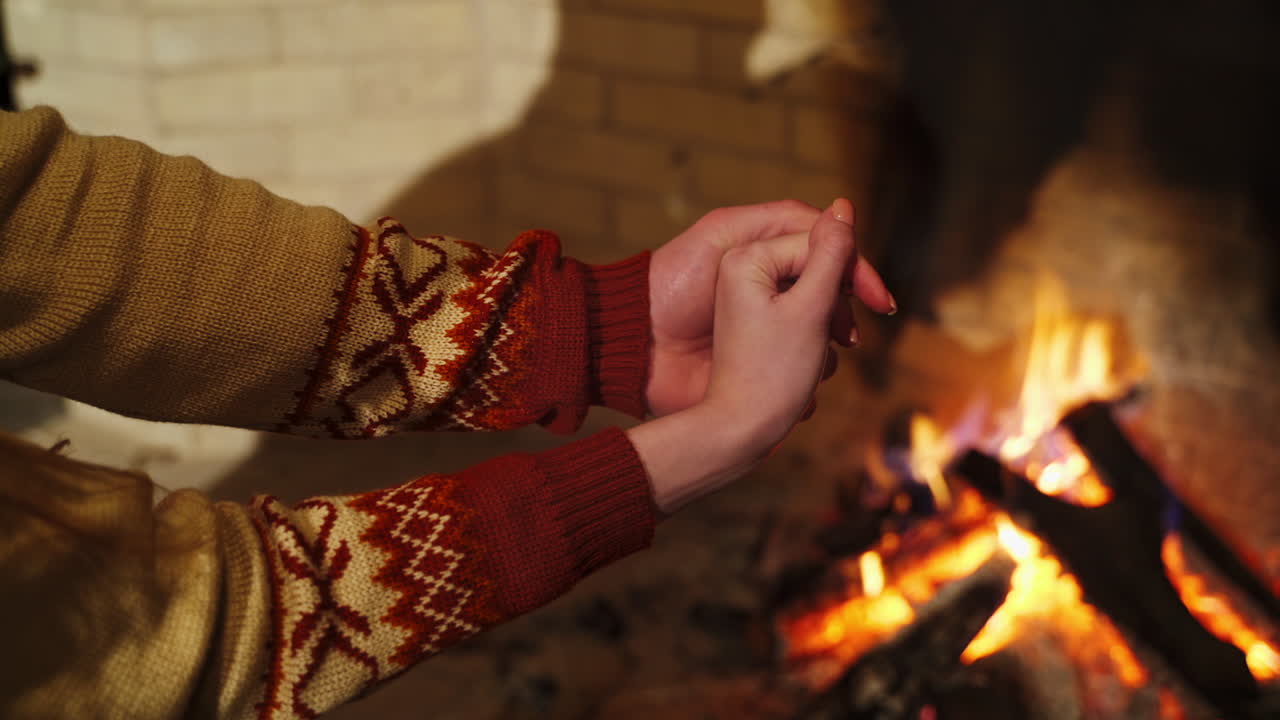Hands of a man and woman near the fireplace. Couple in love warming hands by fireplace indoors. Romantic atmosphere at home.
