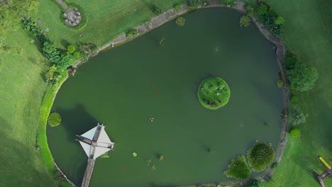 aerial top-down view zooming out from an artificial lagoon with fish. features a small green island in the center surrounded by a walking bridge and greenery. guatemala.