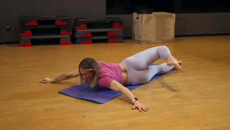 Person lying on a mat in a gym twists legs around back, performing a full body stretch to improve flexibility, mobility, and relaxation