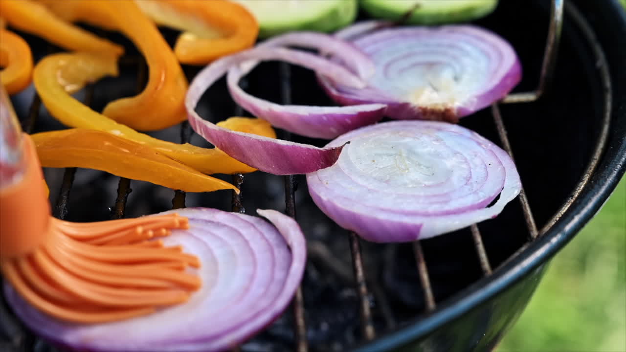 Frying vegetables on a grill at glamping. Corn cobs, bell peppers, onions, zucchinis. Man greases vegetables with oil