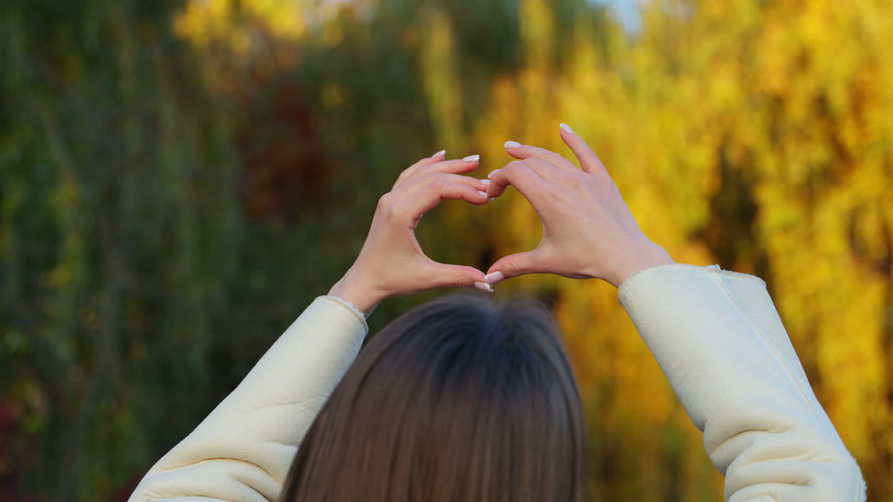 Woman making a heart shape with her hands in an autumn park