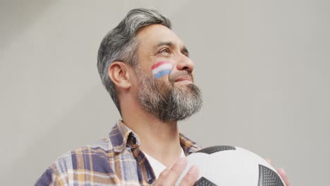 happy biracial man with flag of netherlands on cheek holding football