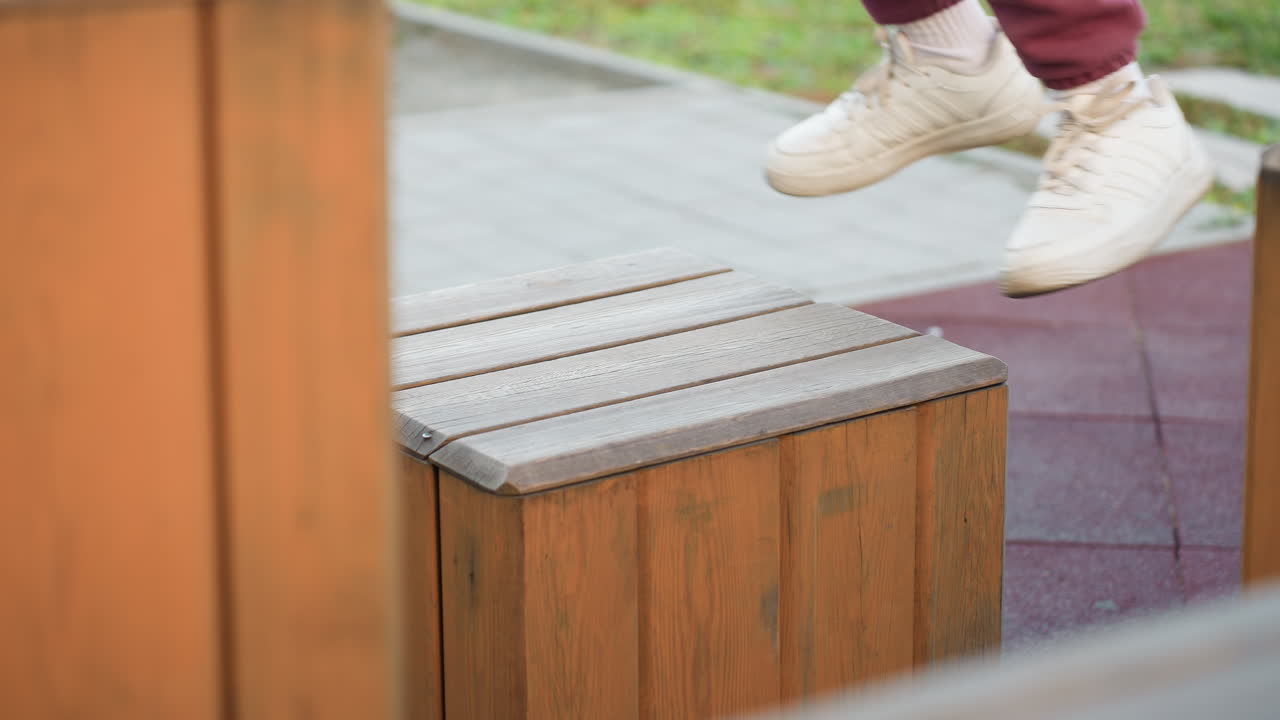 Side view fitness instructor legs stepping onto wooden jump box on white canvas outdoors highlighting balance control strength power during dynamic workout on rubber floor with park background