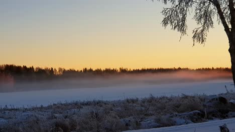 Lapso-De-Tiempo-Del-Lago-Invernal-Congelado-En-Laponia,-Finlandia,-Con-Puesta-De-Sol-Dorada-Iluminando-La-Mística-Niebla-Danzante