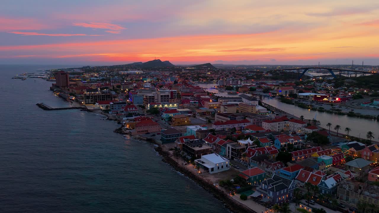 Sunset aerial panoramic descend over Punda and Pietermaai in Curacao, colorful waterfront buildings and calm sea under a vibrant sky