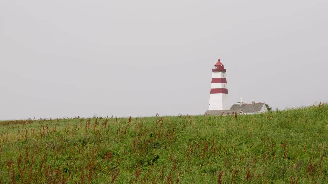 A lighthouse at the norwegian coast. Standing on a hilltop in the grassland.