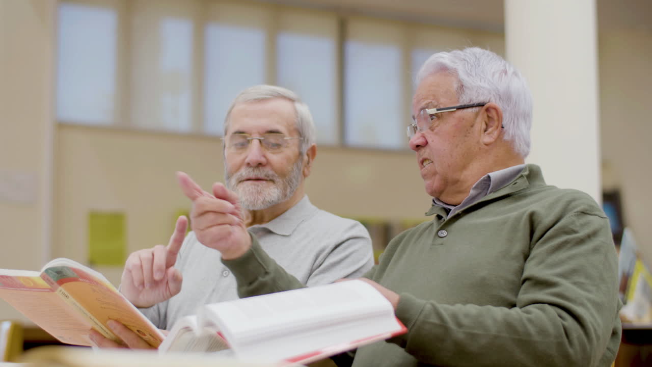 hombres maduros hablando mientras leen libros de texto en la biblioteca