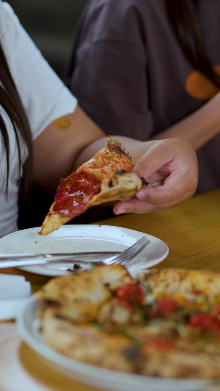Primo piano di mani che sollevano una fetta di pizza fresca al salame piccante da un tavolo di ristorante.