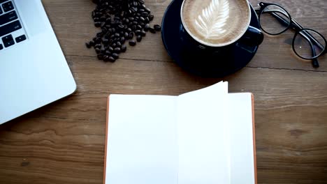 4k footage cinemagraph. blank white book on wooden table, page flip from wind. book at work space with notebook , cup of coffee and glasses