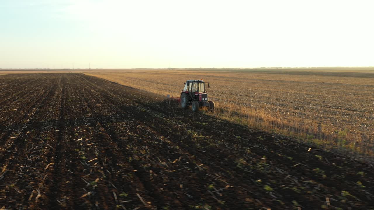 vista lateral aérea de un tractor que arrastra una harra de disco sobre un campo agrícola, tierras de cultivo