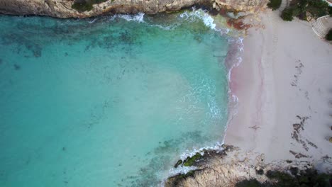 drone rises above turquoise water and white sand beach of cala anguila cove, mallorca