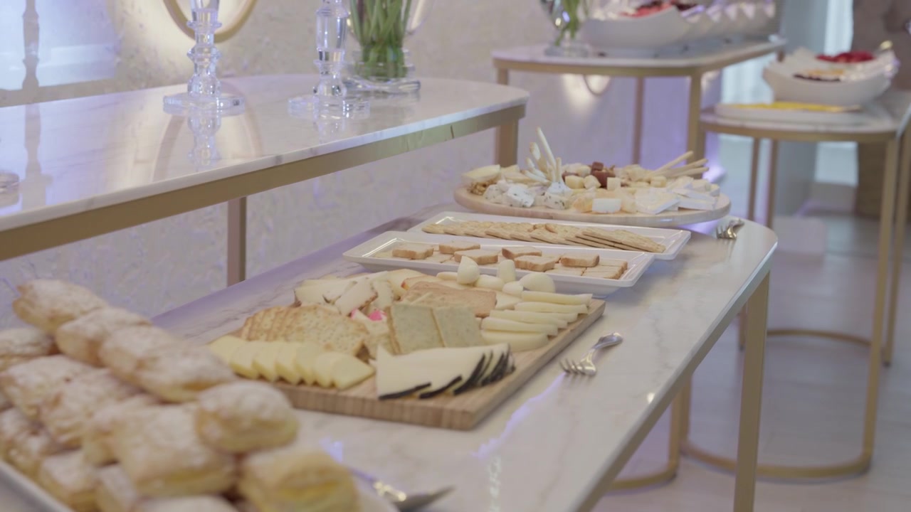 Ostefade, sandwich og pudrede kager anrettet langs en marmorbuffetdisk