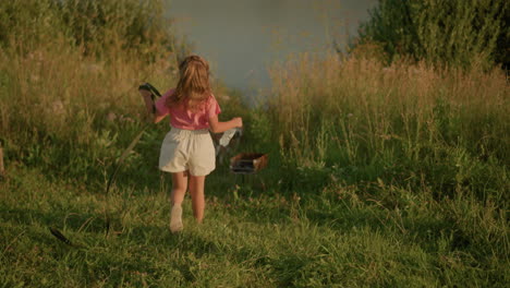 back view of lady in pink shirt running towards dog in lush greenery holding rope in left hand and water bottle in right, natural surroundings with grass and plants