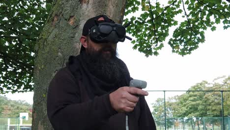 bearded male wearing fpv goggles controlling drone in park with motion joystick