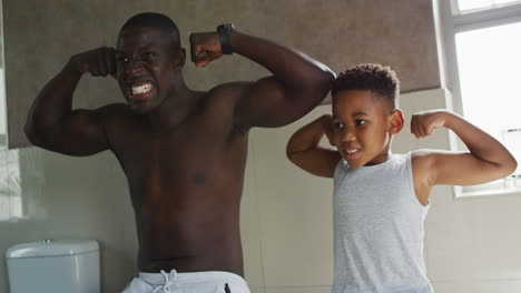video de un feliz padre y hijo afroamericanos mostrando músculos en el espejo