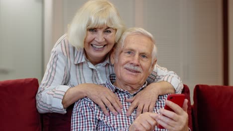 Pareja-De-Abuelos-Mayores-Hablando-Y-Usando-Teléfonos-Móviles-Digitales-En-Casa.-Cierre-De-Emergencia-Por-Coronavirus