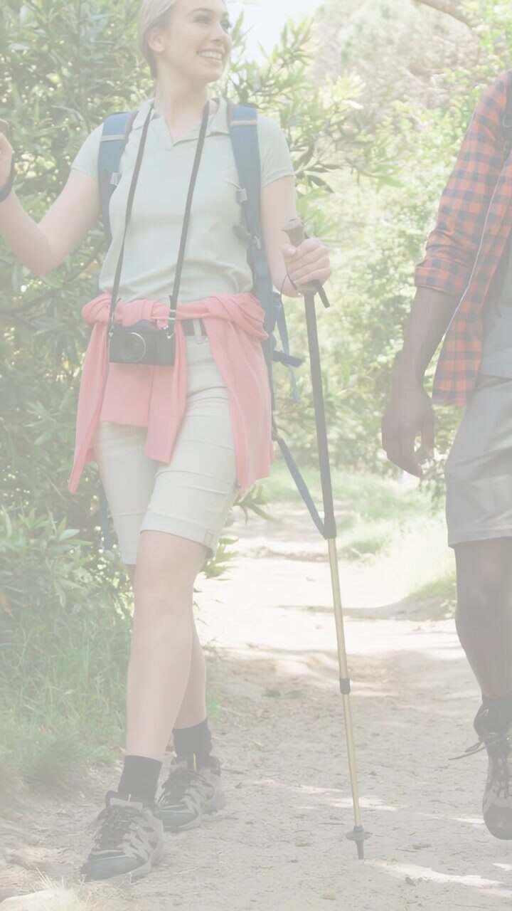 Video verticale: Donna che entra da sinistra camminando con un uomo su un sentiero illuminato dal sole, piantando un bastone da trekking per il viaggio.