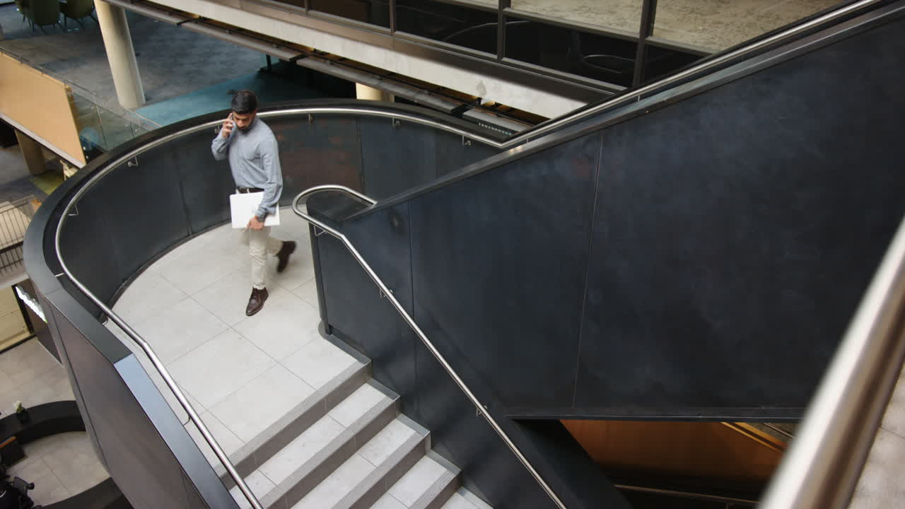 Walking down stairs, businessman talking on smartphone in modern office building