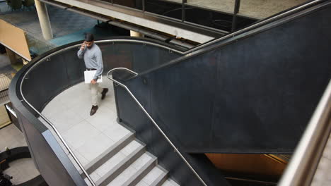 walking down stairs, businessman talking on smartphone in modern office building