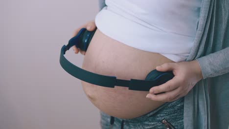 pregnant lady with headphones on tummy dances at light wall