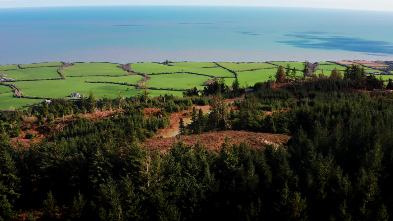 Kretsande flygvy av Tara Hill omgiven av gröna fält, skog och hav i bakgrunden.
