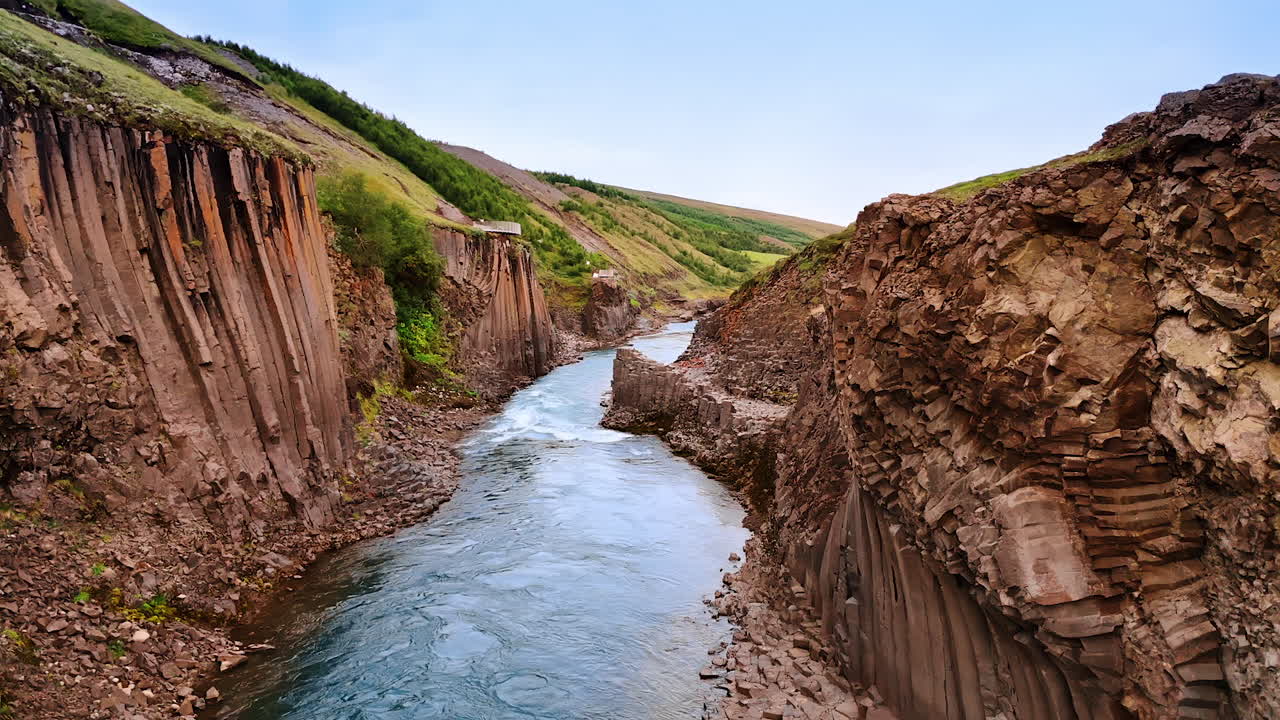 Stunning columnar rocks with green grass on top. Tourists walk by the mountains. River flows at the foot of the cliffs. Iceland scenery.