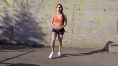 young latina woman doing forward lunges outdoors, front view