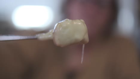 fondue - hand turns a piece of baguette bread with melted hot cheese, close up