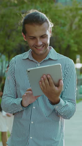 young man smiling while using a tablet outdoors