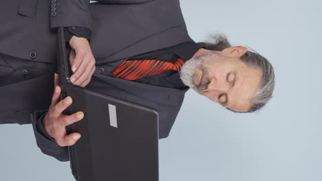 vertical video of old businessman looking at laptop with tired expression.