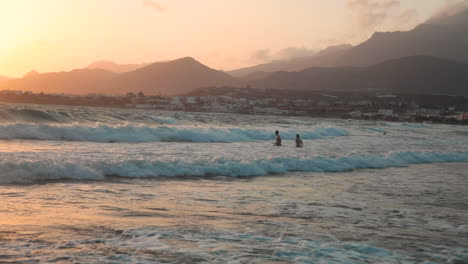silhouette of people playing in the waves during a warm sunset.