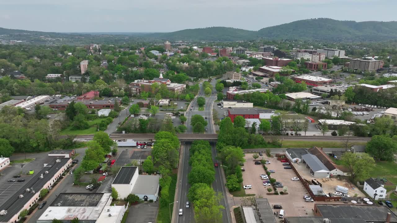 Traffic on main street of Charlottesville. Factory And Company Buildings with railway bridge. Rising drone wide shot. Downtown skyline with mountains in distance.
