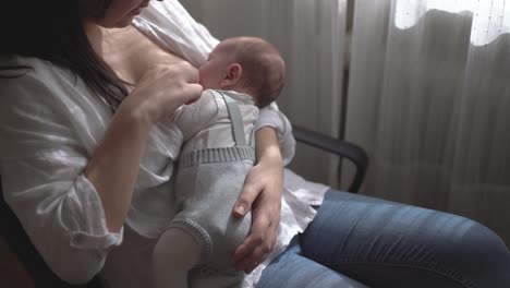 mother breastfeeding newborn baby in armchair at home