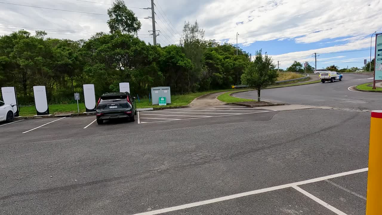 Tesla vehicles parked and charging at a Coffs Harbour supercharger station under bright daylight, surrounded by greenery