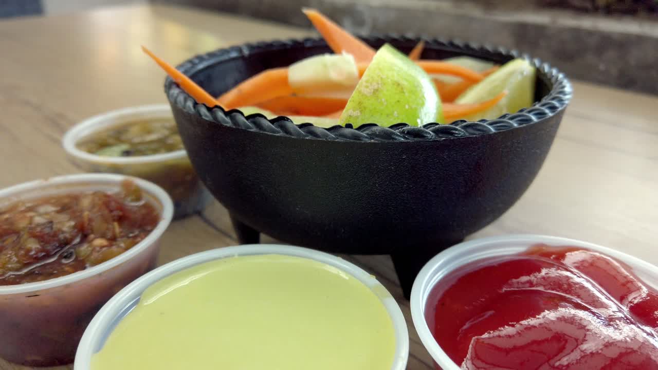 Zoom out shot of traditional Mexican pickled vegetables with cucumber, carrot, and lime in black molcajete bowl